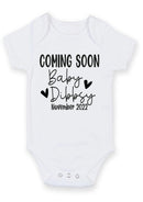 Flat mockup of the baby coming soon design on a short-sleeve baby vest