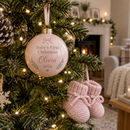 Baby's first Christmas bauble hanging on a Christmas tree beside knitted booties