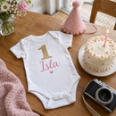 Personalised cake smash outfit with the name Isla laid out with a first birthday cake