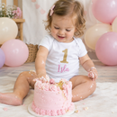 Toddler in a personalised cake smash outfit with the name Isla at a first birthday photo shoot