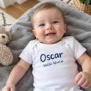 Baby wearing a personalised baby vest printed with Oscar and Hello World