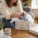 Parent filling a personalised baby keepsake box with baby's first shoes