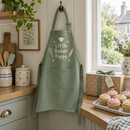 Personalised kids apron printed Little Baker Poppy hanging in a kitchen beside a gift