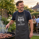 Man at a garden barbecue wearing a personalised apron printed Dave's BBQ