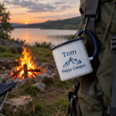 Personalised enamel camping mug with the name Tom on a backpack by a campfire