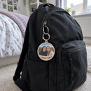 Personalised double-sided keyring: a teenage girl's school rucksack on a bedroom floor in a UK home with a personalised round double-sided wooden keyring clipped to the zip