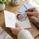 Personalised photo fridge magnet: a personalised flexible heart photo magnet with a newborn baby photo and the name 'Freddie' being slipped into a greetings card on a table with an envelope and pen