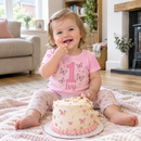 Baby girl wearing a personalised first birthday age t-shirt at her cake smash