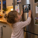Personalised musical photo magnet: a young child standing on tiptoe pressing a personalised black musical photo magnet on a family fridge printed with a photo of their dad in work clothes and the words 'Night night, Daddy'