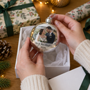 Personalised photo bauble: hands lifting a personalised silver mirror-finish photo bauble with a couple's wedding photo and the words 'Mr & Mrs Hughes 2026' out of a white gift box on a table