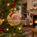 Personalised photo bauble: a personalised gold mirror-finish photo bauble showing a newborn baby in a Santa hat and the text 'Baby's First Christmas 2026 - Olivia' hanging on a real Christmas tree