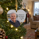 Personalised metal Christmas decoration: a personalised heart-shaped metal Christmas ornament printed with an older man's photo and the words 'Forever in our hearts - Grandpa' hanging on a Christmas tree