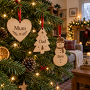 Personalised wooden Christmas decorations in heart, tree and snowman shapes printed with 'Mum', 'Dad' and 'Ben' hanging on a Christmas tree