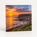 Personalised metal photo print printed with a dramatic sunset photo over a Yorkshire coastline and a small caption Robin Hood's Bay 2025, on a plain background