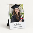 Personalised desk photo panel printed with a graduation photo of a young woman in cap and gown and the text Chloe and Graduated 2026, on a plain background