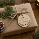 Personalised wooden Christmas decoration: a brown-paper wrapped present tied with string and a personalised round wooden Christmas decoration used as a gift tag, printed with the words 'To Miss Clarke, love Daisy'