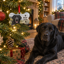 Personalised pet's first Christmas decoration: a personalised dog bone Christmas ornament printed with a photo of a black labrador and the name 'Bear 2026' hanging on a Christmas tree with a real black labrador