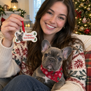 Personalised pet's first Christmas decoration: young woman holding a dog bone photo ornament reading 'Pudding's First Christmas' with her French bulldog puppy