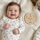 Baby with a personalised baby milestone wooden disc for monthly photos