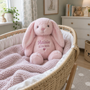 Personalised bunny rabbit soft toy: a pink plush bunny rabbit soft toy printed with the name 'Maisie' and a date of birth sitting in a wicker Moses basket with a knitted blanket in a calm British nursery