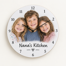 Personalised photo wall clock with the face printed with a photo of three smiling grandchildren and the text Nana's Kitchen, on a plain background