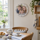 Personalised photo wall clock, hanging on a bright UK farmhouse kitchen wall above a table set for tea