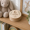 Personalised baby milestone wooden discs on a nursery shelf