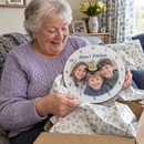 Personalised photo wall clock, being unwrapped by a delighted grandmother in her 70s on a sofa