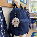Personalised mini bunny keyring: a child's navy school rucksack hanging on a classroom peg in a UK primary school with a personalised mini plush bunny keyring clipped to the zip printed with the name 'Sophie'