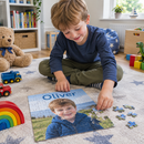 Personalised kids jigsaw: a young boy aged about five sitting on a playroom rug putting together a personalised 30 piece jigsaw of himself with the name 'Oliver' across the top