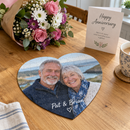 A personalised heart jigsaw with a photo of an older couple and the names 'Pat & Brian' completed on a kitchen table next to an anniversary card and a bunch of flowers
