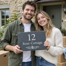 Personalised slate house sign with the name Rose Cottage held by a couple outside their new home