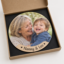 Personalised wooden jigsaw: a completed personalised round MDF wooden jigsaw puzzle, 24 pieces with visible cut lines, printed with a photo of a grandmother and toddler laughing and the name 'Nanny & Leo'