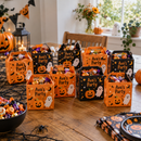 Halloween treat boxes with the name Ava's Party filled with sweets on a party table