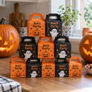 Halloween treat boxes with the name Ava's Party stacked beside carved pumpkins