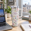 White stainless steel tumbler with a name and floral pattern on a home office desk