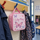 Pink lunch bag with a butterfly name panel on a school coat peg