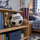 Personalised football with team name on a bedroom shelf beside trophies and medals