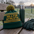 Knitted bobble hat with team name on a bench beside a flask and gloves