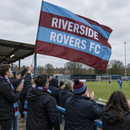 Fans on a terrace waving a large custom stadium flag with their team name