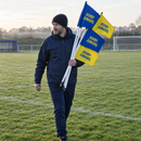 Coach carrying a set of custom football corner flags across the pitch before kick-off