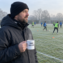 Grassroots coach on the touchline holding a thank you coach mug