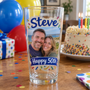 Pint glass with a couple's colour photo and Happy 50th on a birthday table