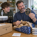 Dad unwrapping a pump clip reading 'Dad's Best Stout' beside his home-brew kit