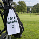 Hole in one golf towel hanging from a golf bag beside a par 3 green