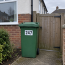 Personalised wheelie bin sticker on a green bin beside a garden gate
