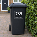 Personalised wheelie bin sticker on a black bin by a hedge