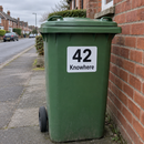 Personalised wheelie bin sticker on a green bin by a brick wall