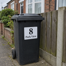 Personalised wheelie bin sticker on a black bin by a garden fence