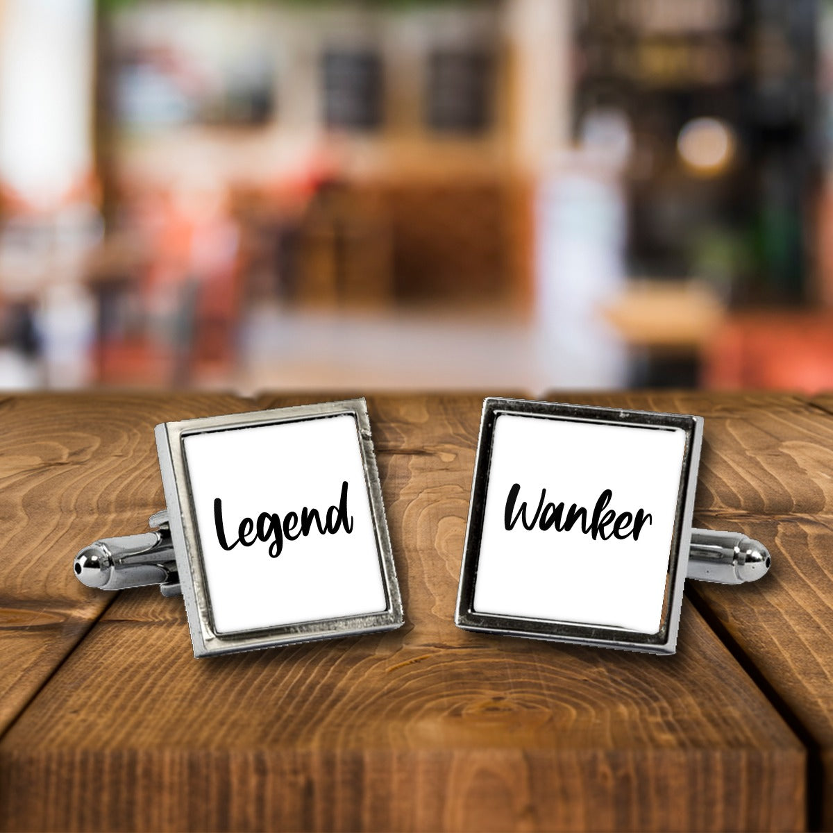 Legend Wanker Cufflinks – Rude Novelty Cufflinks for Men – White or Black Print, Chrome or Rose Gold – Legend Wanker cufflinks, a chrome square pair with white print on a wooden bar table